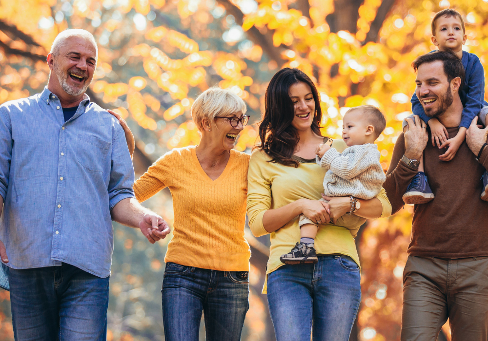 Дядо, баба, мама с бебе, баща с баткото на конче вървят на фона на дървета с есенни жълти листа.