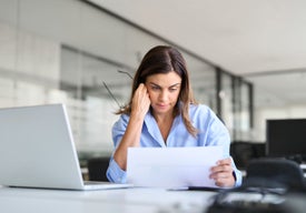 Žena u počítače se dívá na kus papíru