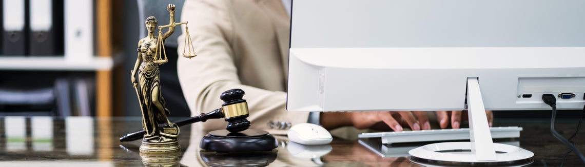 Човек на компютър, до чийто монитор има фигурка на Темида и съдийско чукче.