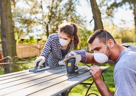 Muž a žena s maskami na tvári používajú brúsku na piknikovom stole