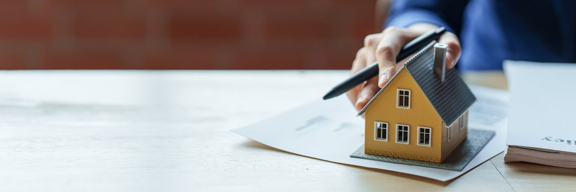 Osoba držiaca pero nad malým modelom domu