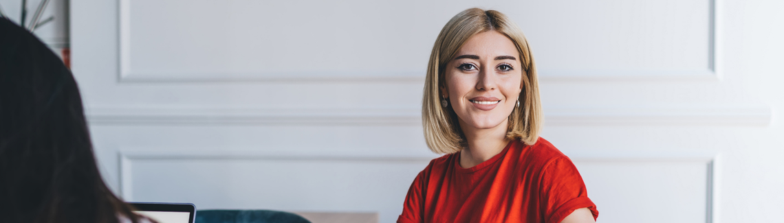 Egy nő egy asztalnál ül egy noteszgéppel és egy tollal.