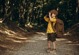 Chlapec se dívá dalekohledem na stezce mezi stromy.
