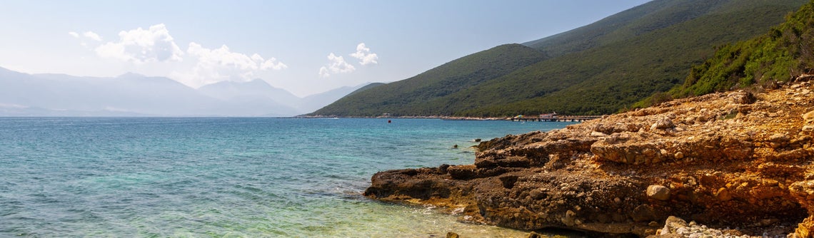 Skalnaté pobřeží s velkou vodní plochou a kopcem v pozadí