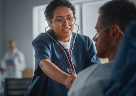 Žena s brýlemi a stetoskopem kontrolující pacienta na lůžku
