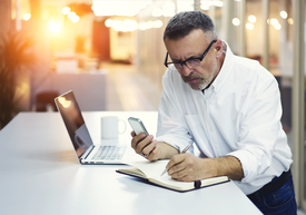 Un bărbat stă la o masă cu un laptop și un telefon