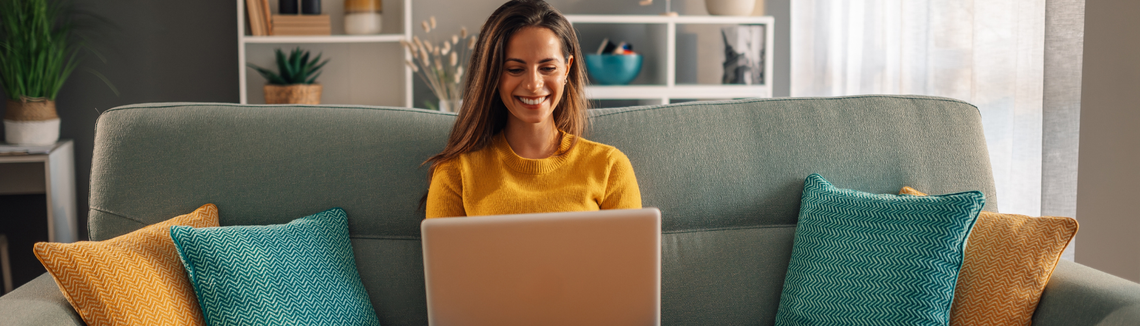 Egy nő ül egy kanapén egy laptop előtt.