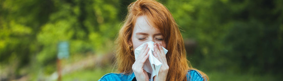 Žena smrká do kapesníku venku v přírodě