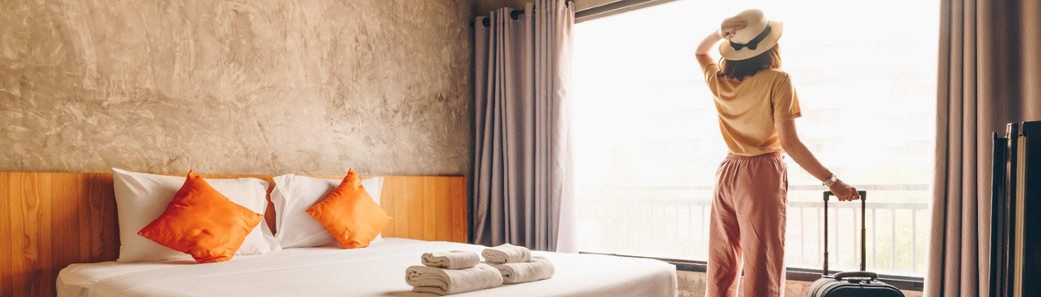 Egy nő áll a hotelszobában bőrönddel