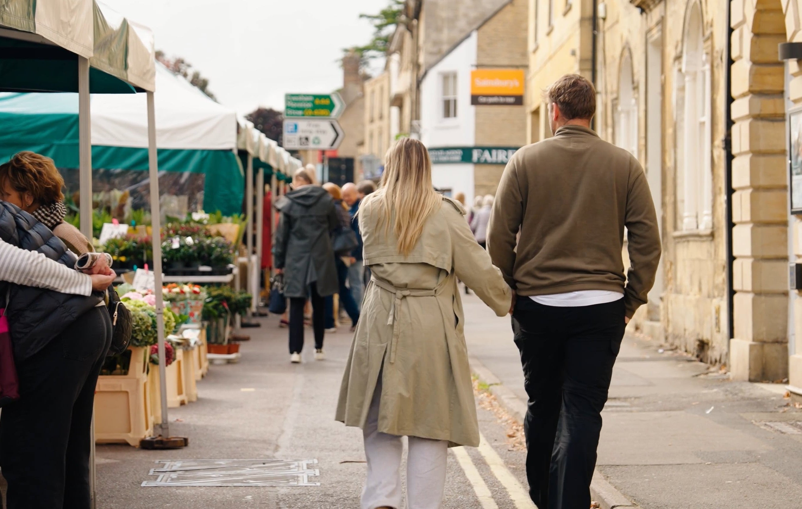 Couple walking through Chipping Norton market, passing local stalls and independent shops in the town centre.