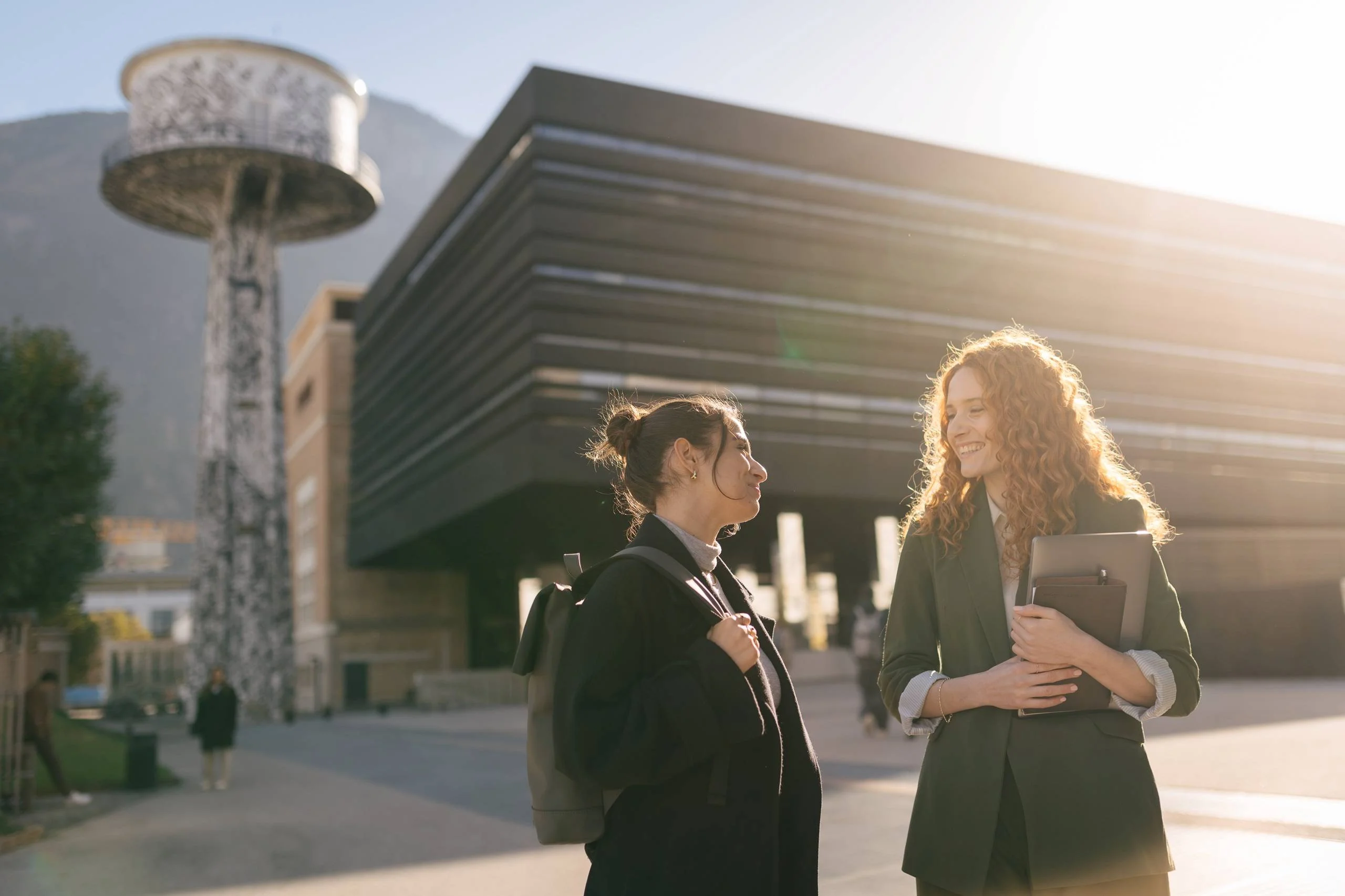 Two young women talking in front of a modern building and a water tower