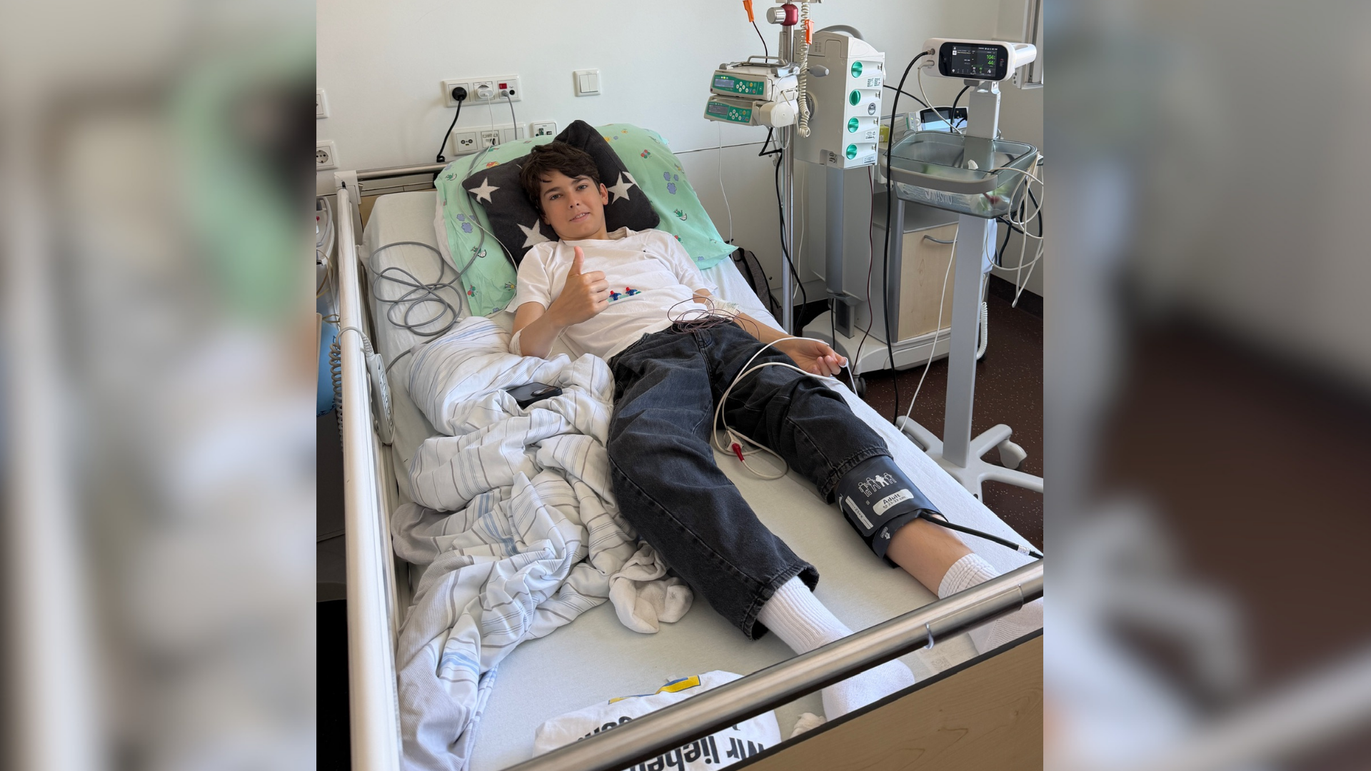 Ein Junge liegt in einem Krankenhausbett und zeigt den Daumen nach oben.