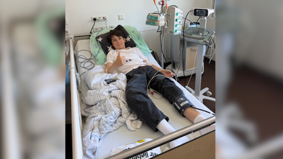 Ein Junge liegt in einem Krankenhausbett und zeigt den Daumen nach oben.