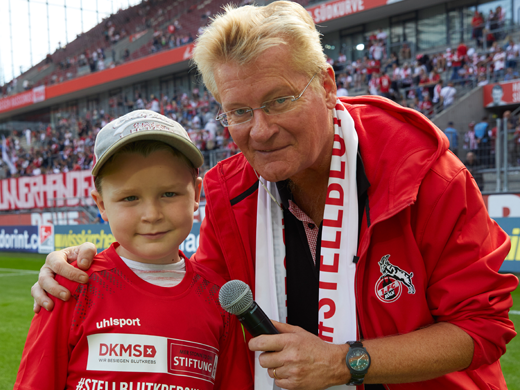 Ein Mann mit Mikrofon steht neben einem Jungen, beide in FC Merch