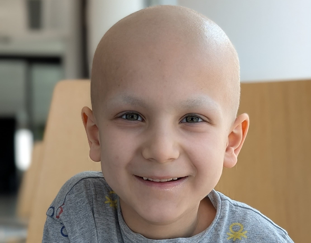 Ein krebskrankes Kind mit Glatze lächelt in die Kamera. 