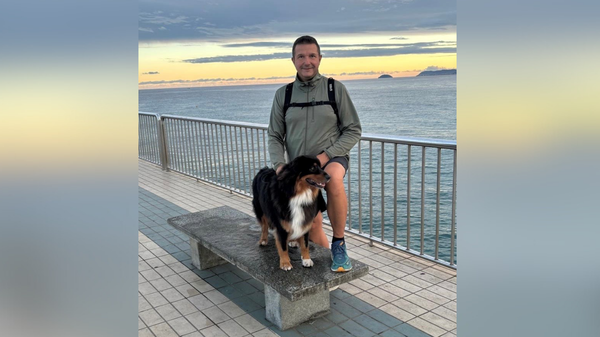 Ein Mann steht mit einem Hund vorm Meer.