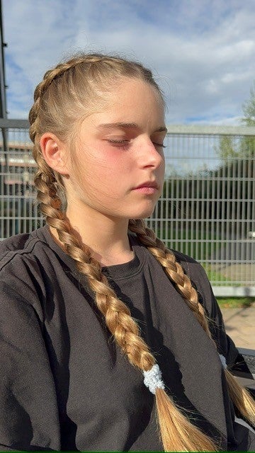 Patientin Julie sitzt mit geflochtenem Haar draußen und hat die Augen geschlossen.