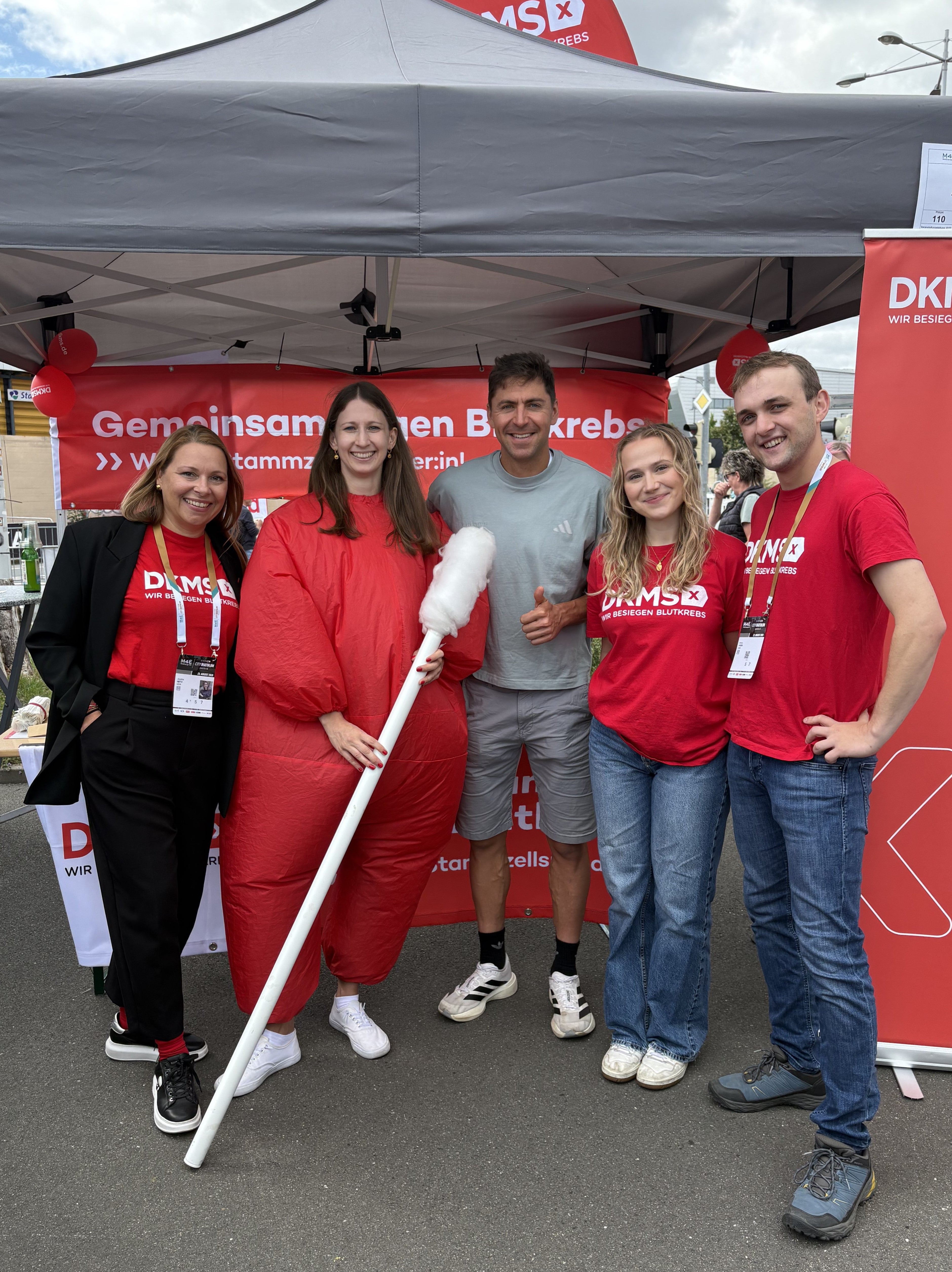 Eine Gruppe von Menschen, die an einem DKMS Stand für ein Foto posieren.