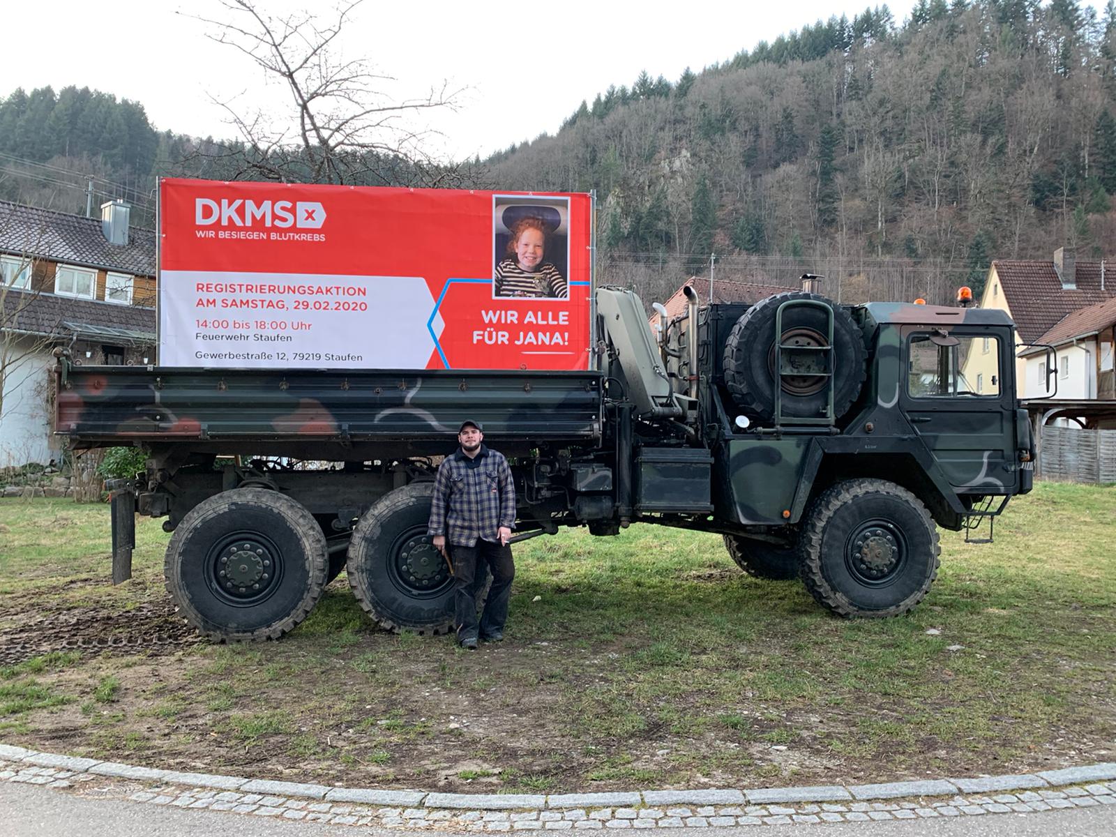 Ein Mann steht neben einem großen Lastwagen, darauf ist ein Plakat mit einem Registrierungsaufruf 