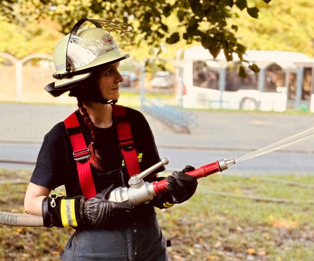 Eine Frau in Feuerwehrmontur hält einen Wasserschlauch in den Händen. 