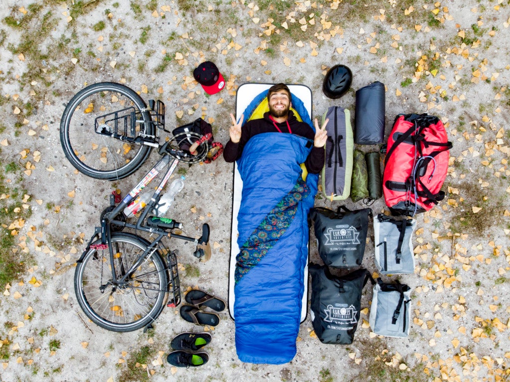 Ein Mann liegt in einem Schlafsack neben einem Fahrrad. Das Foto wurde von oben aus der Luft gemacht. 