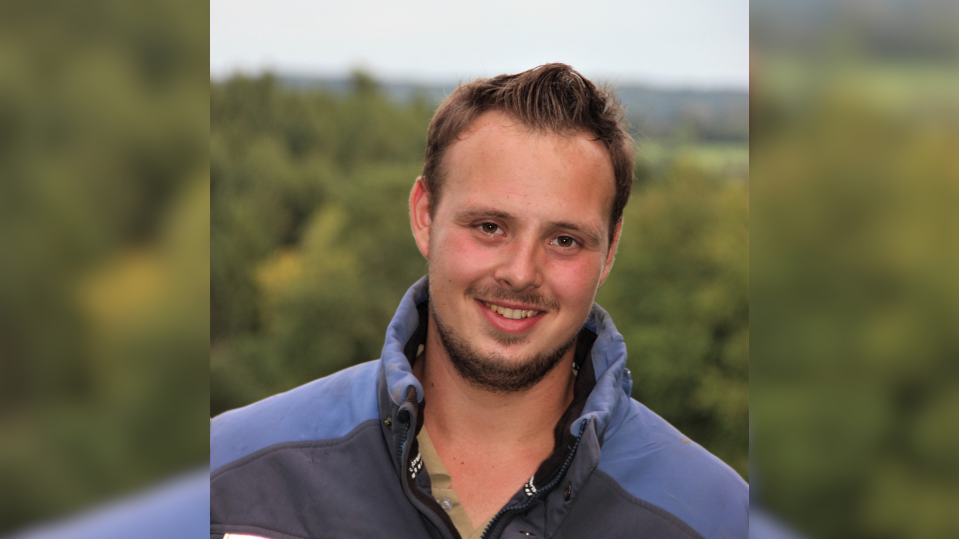 Ein junger Mann trägt eine blaue Jacke und lächelt. 