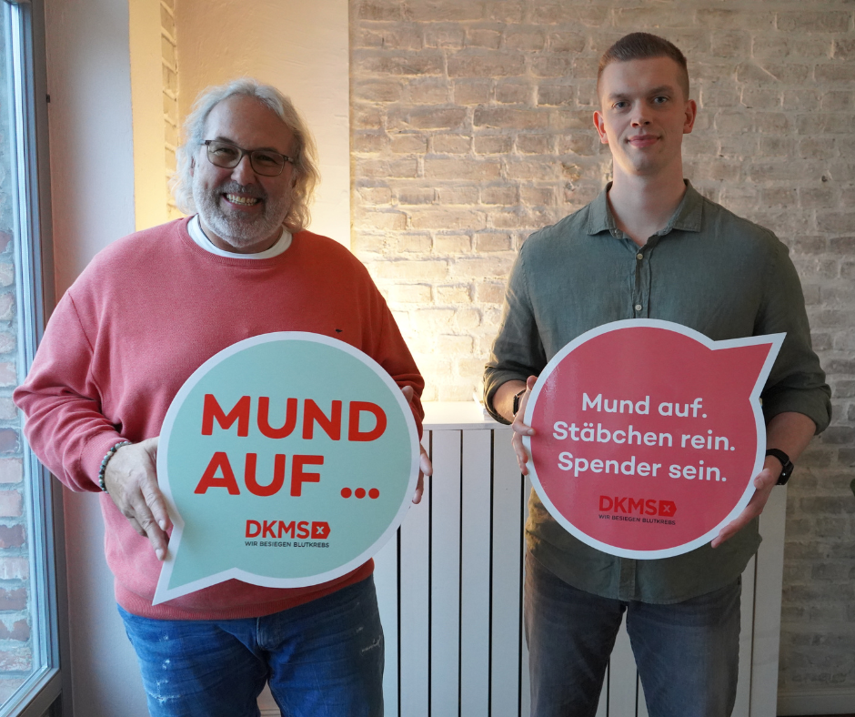 Zwei Männer halten Schilder vor einer Backsteinmauer