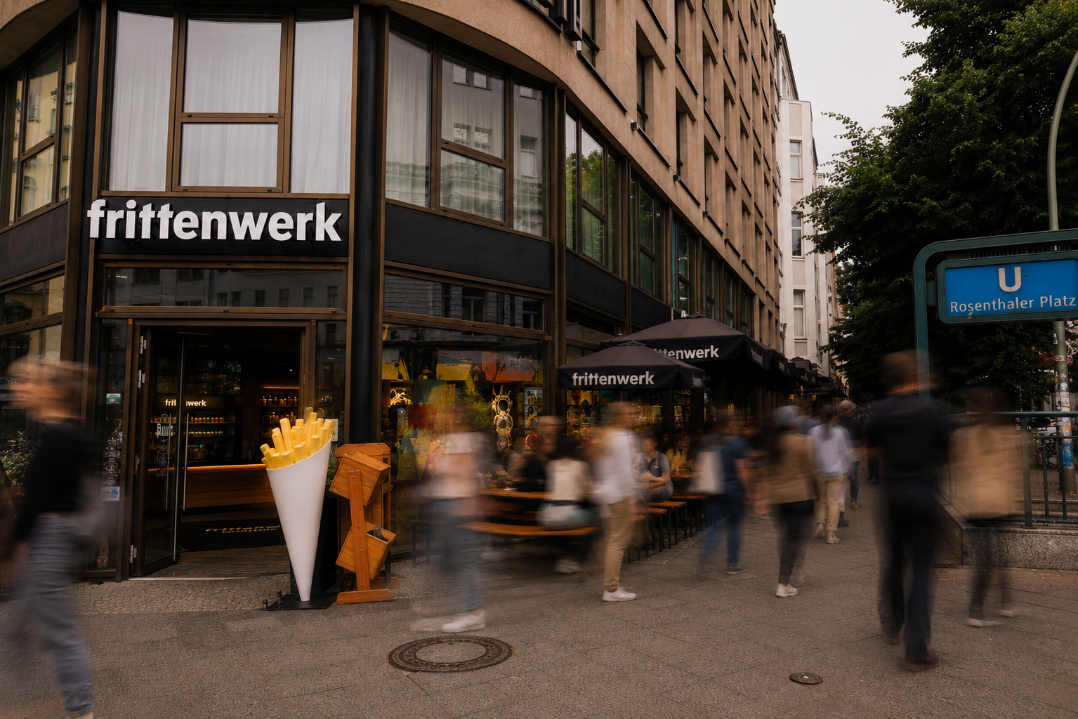 Zu sehen ist eine Filiale von Frittenwerk von außen. Einige Menschen sitzen im Außenbereich und essen.