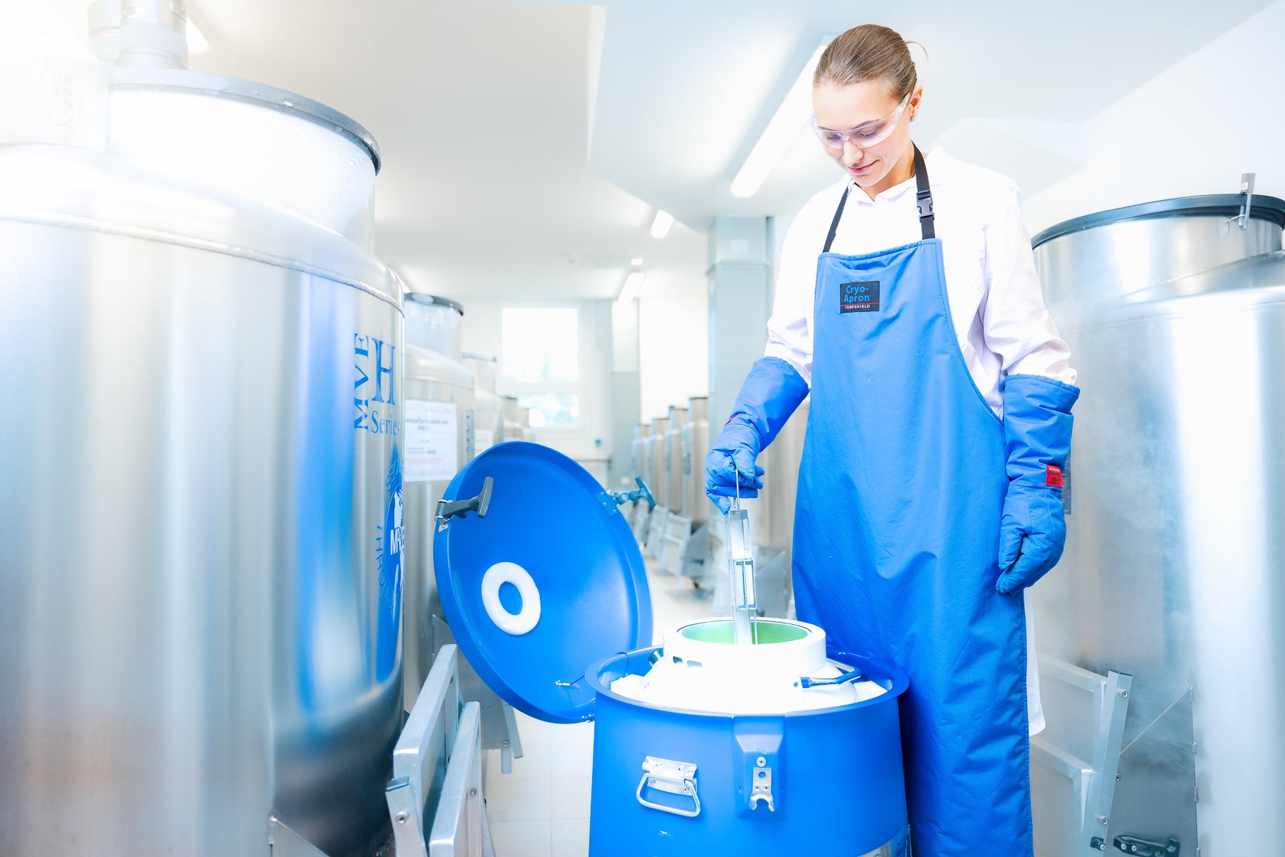 Eine Frau mit einer blauen Schürze und einer Schutzbrille vor einem Kanister