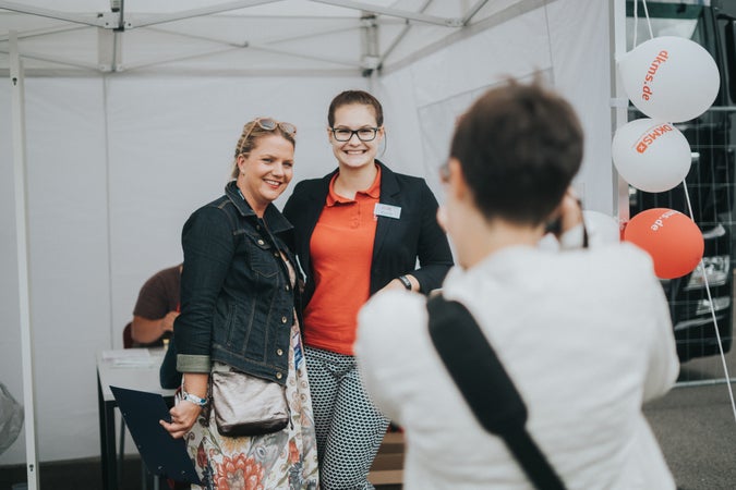 Zwei Frauen, die lächeln und ein Foto machen. Sie stehen nebeneinander und haben die Arme umeinander gelegt.
