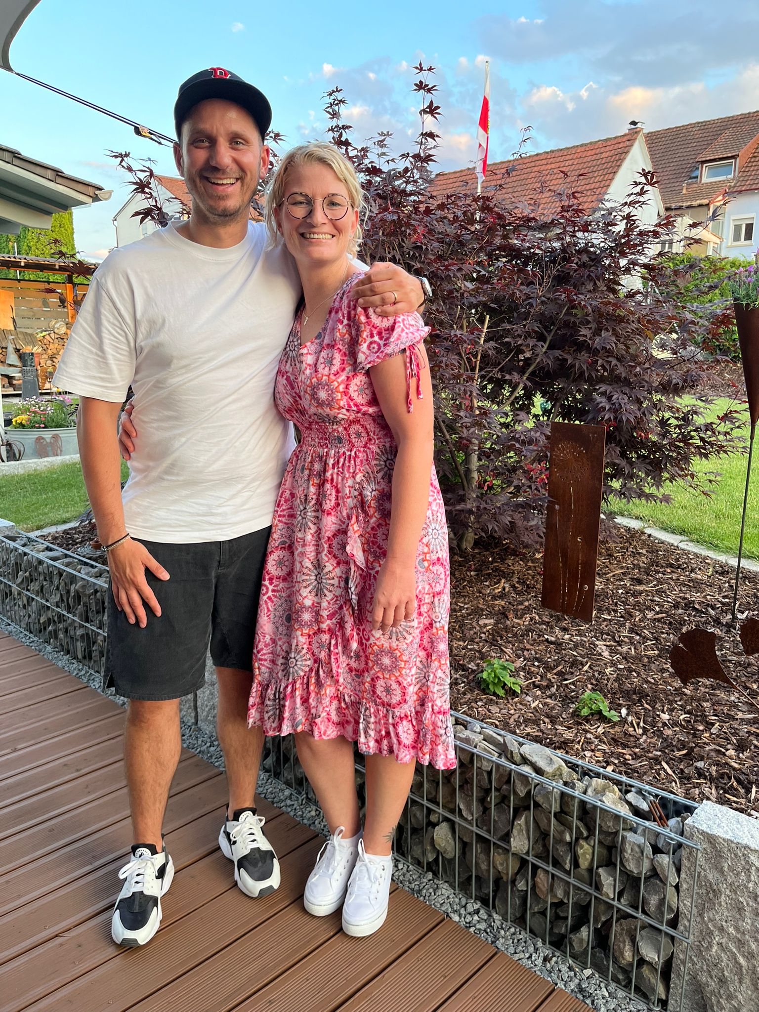 ein Mann und eine Frau stehen nebeneinander in einem Garten und posieren für ein Foto