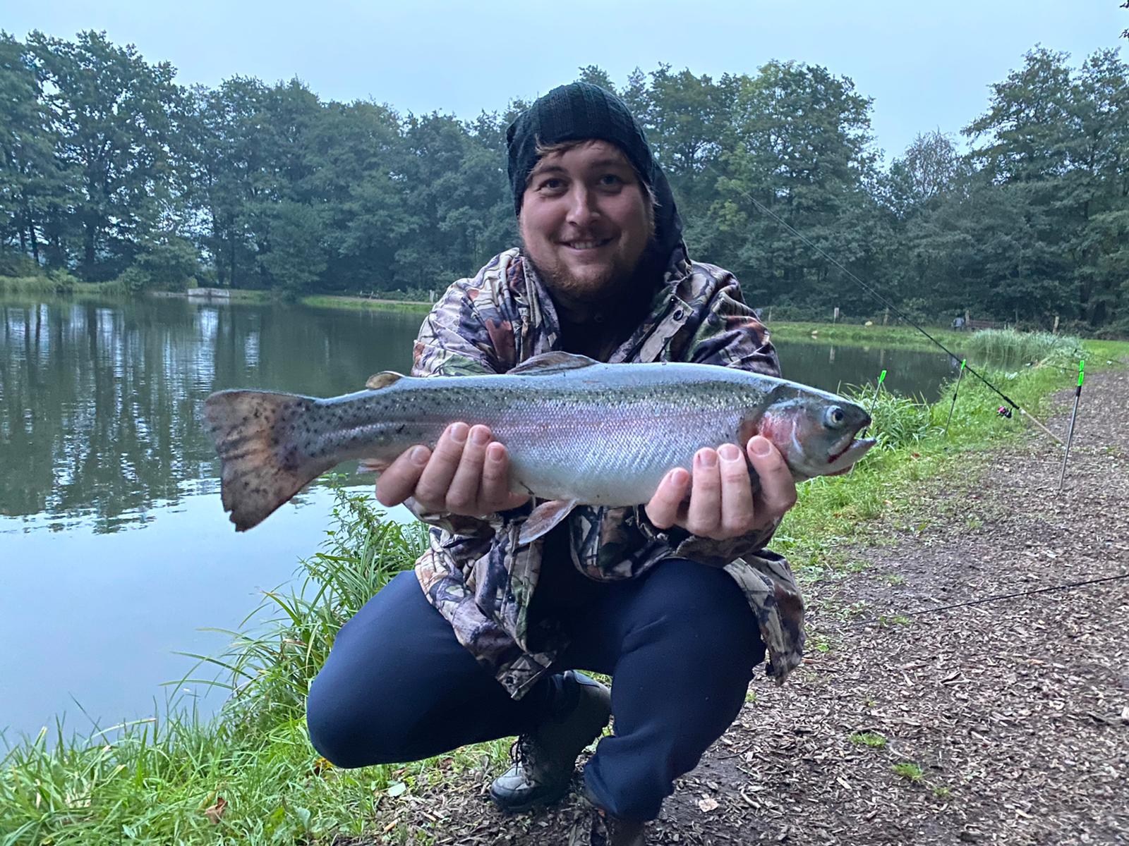 ein Mann posiert mit einem Fisch an einem Teich
