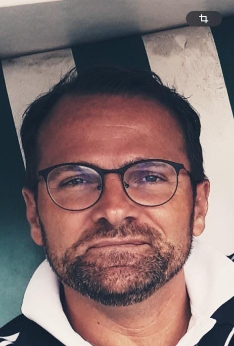 ein Mann mit Bart und Brille lächelt in die Kamera