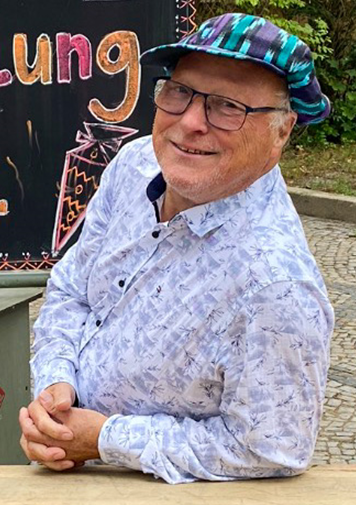 Patient Karl steht im Freien an einen Tisch gelehnt und lächelt fröhlich in die Kamera.