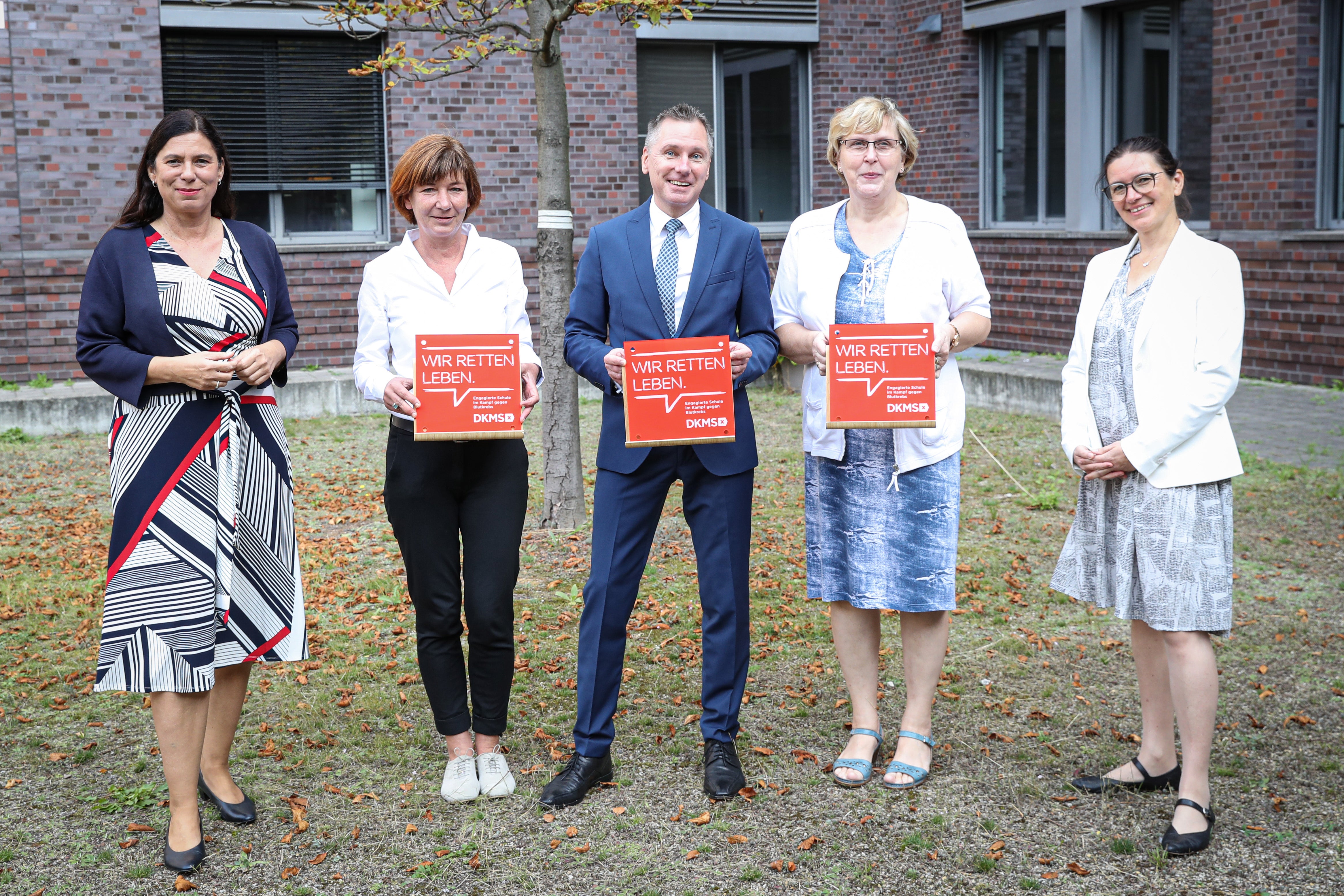 v.l. Sandra Scheeres, Wenke Reimer, Jürgen Dietrich, Sibylle Kucharzewski, Konstanze Burkard, sie posieren vor einem Gebäude und halten Tafeln mit der Aufschrift: "Wir retten Leben" in der Hand