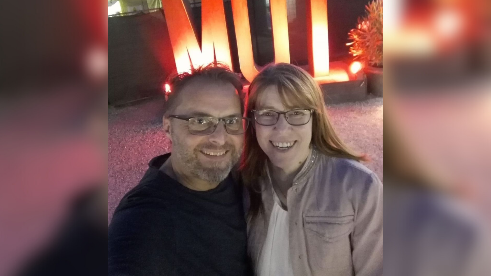 Eine Frau und ein Mann stehen vor einer beleuchteten Schriftskulptur, die "Mut" liest.