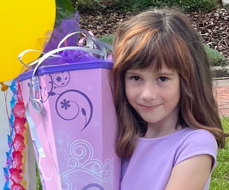 ein Mädchen posiert mit lila Schultüte und lila Kleid für die Kamera