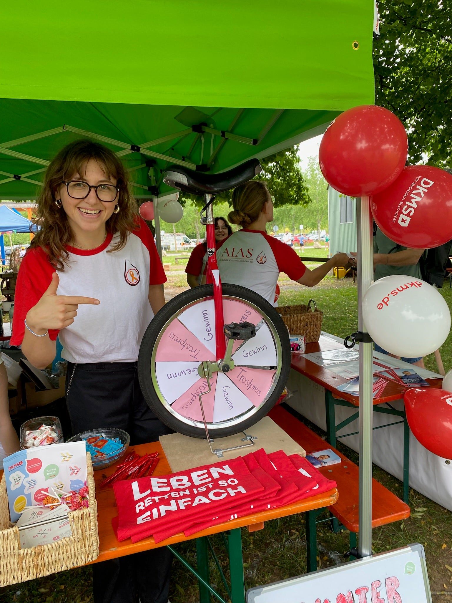 Frau an Stand mit Goodies, Glücksrad, Luftballons und Pavillon