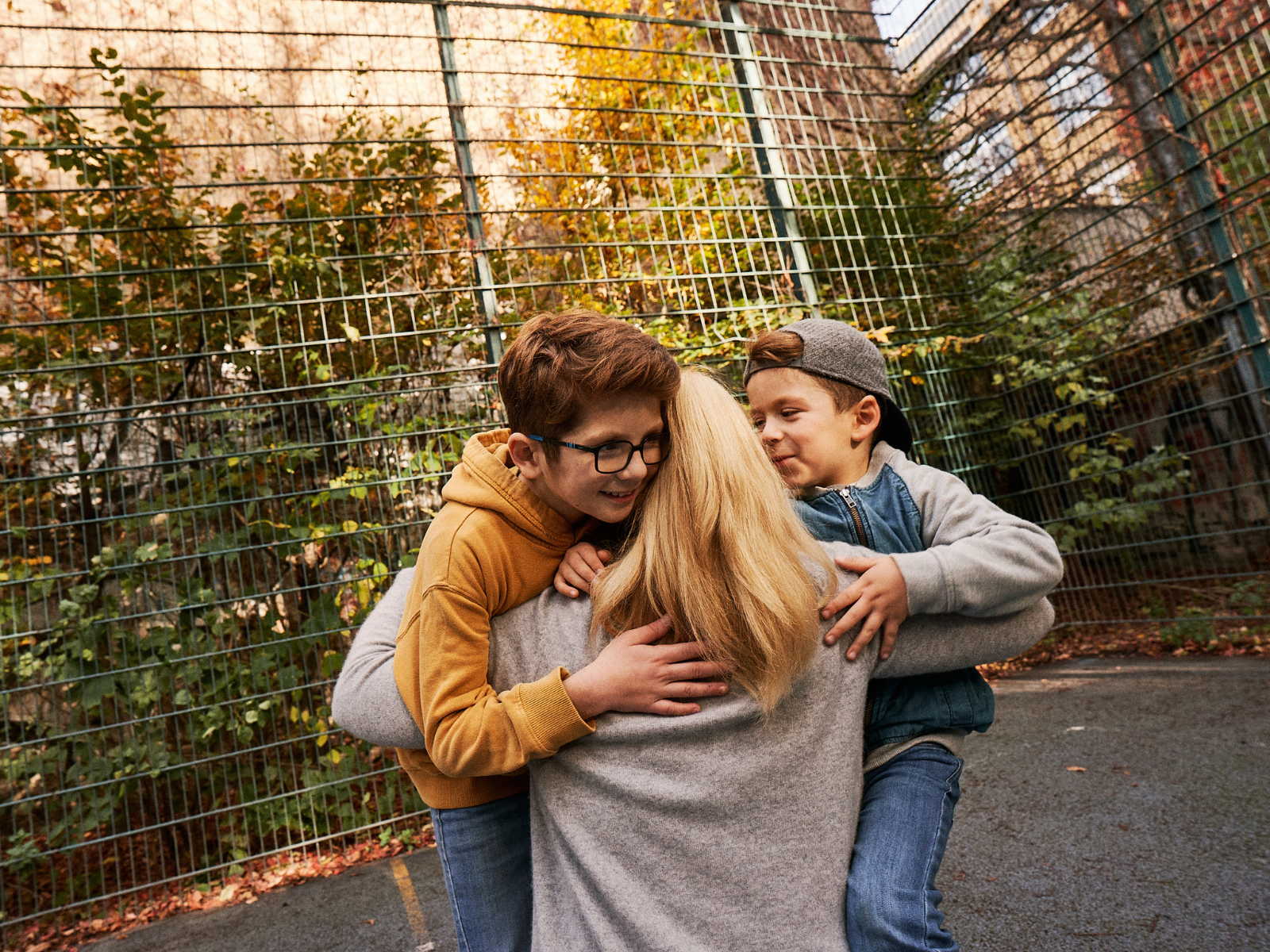 Zwei Jungen umarmen eine Frau auf einem Sportplatz