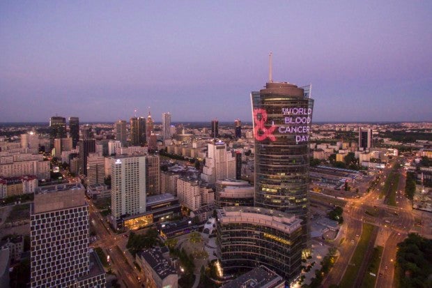Eine Stadtsilhouette mit einem hohen Gebäude, auf dem mit Licht World Blood Cancer Day projiziert ist