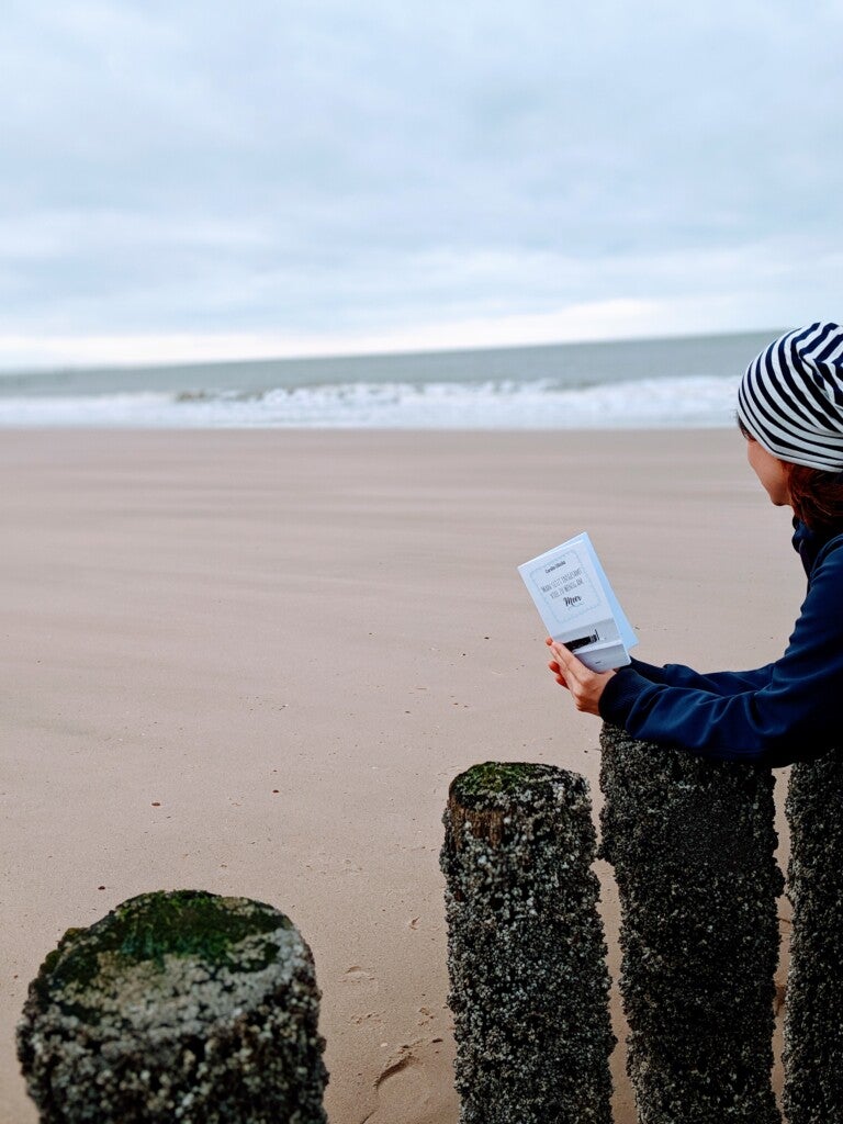 Eine Frau hält ein Buch an einem Strand