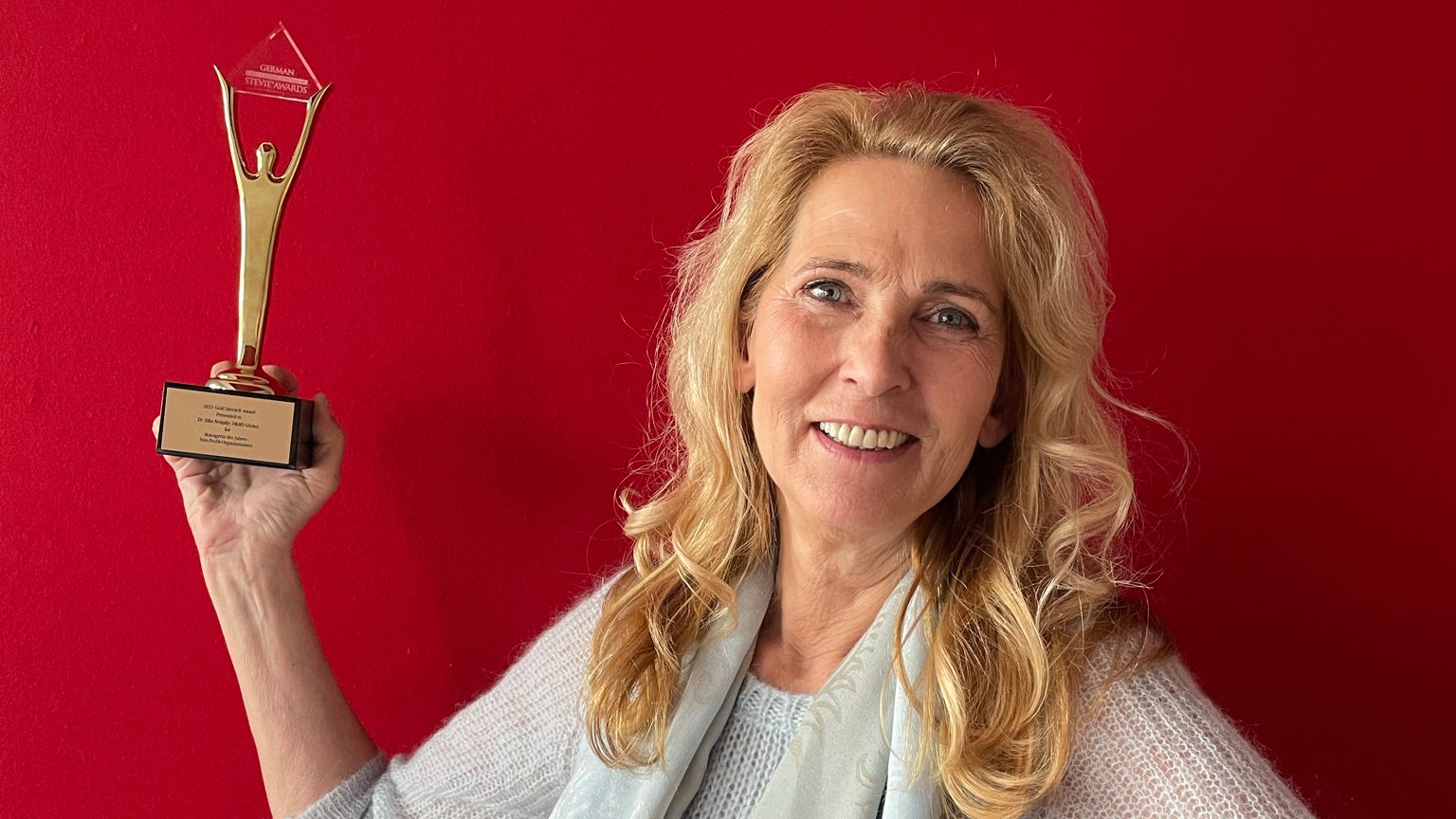 Eine Frau hält einen goldenen Preis hoch und lächelt in die Kamera