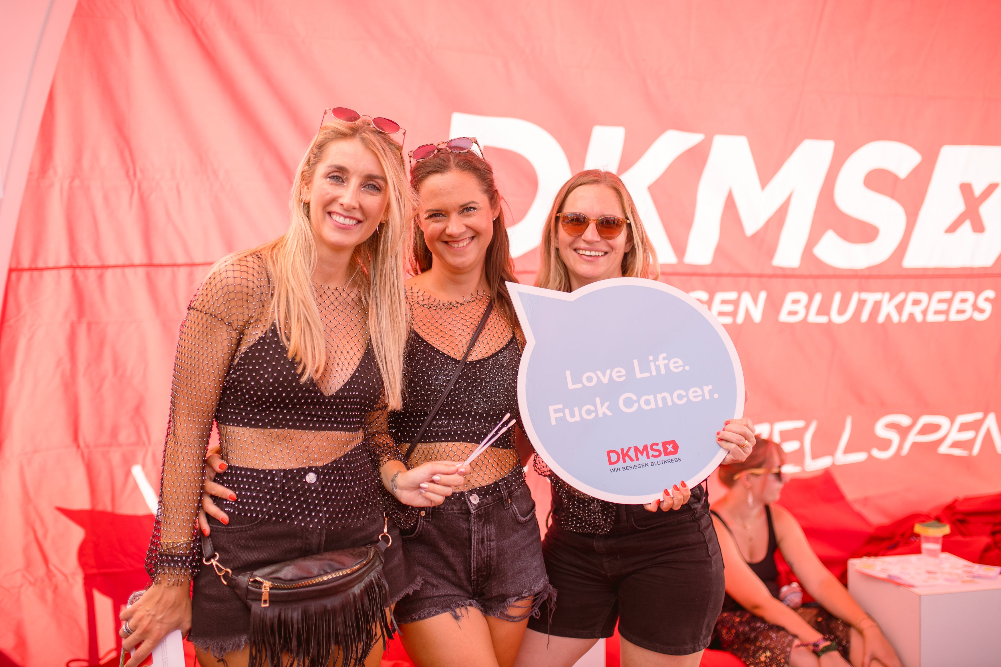 Eine Gruppe von Frauen posiert für ein Foto, ein Schild mit der Aufschrift: Karma Boost wird hochgehalten