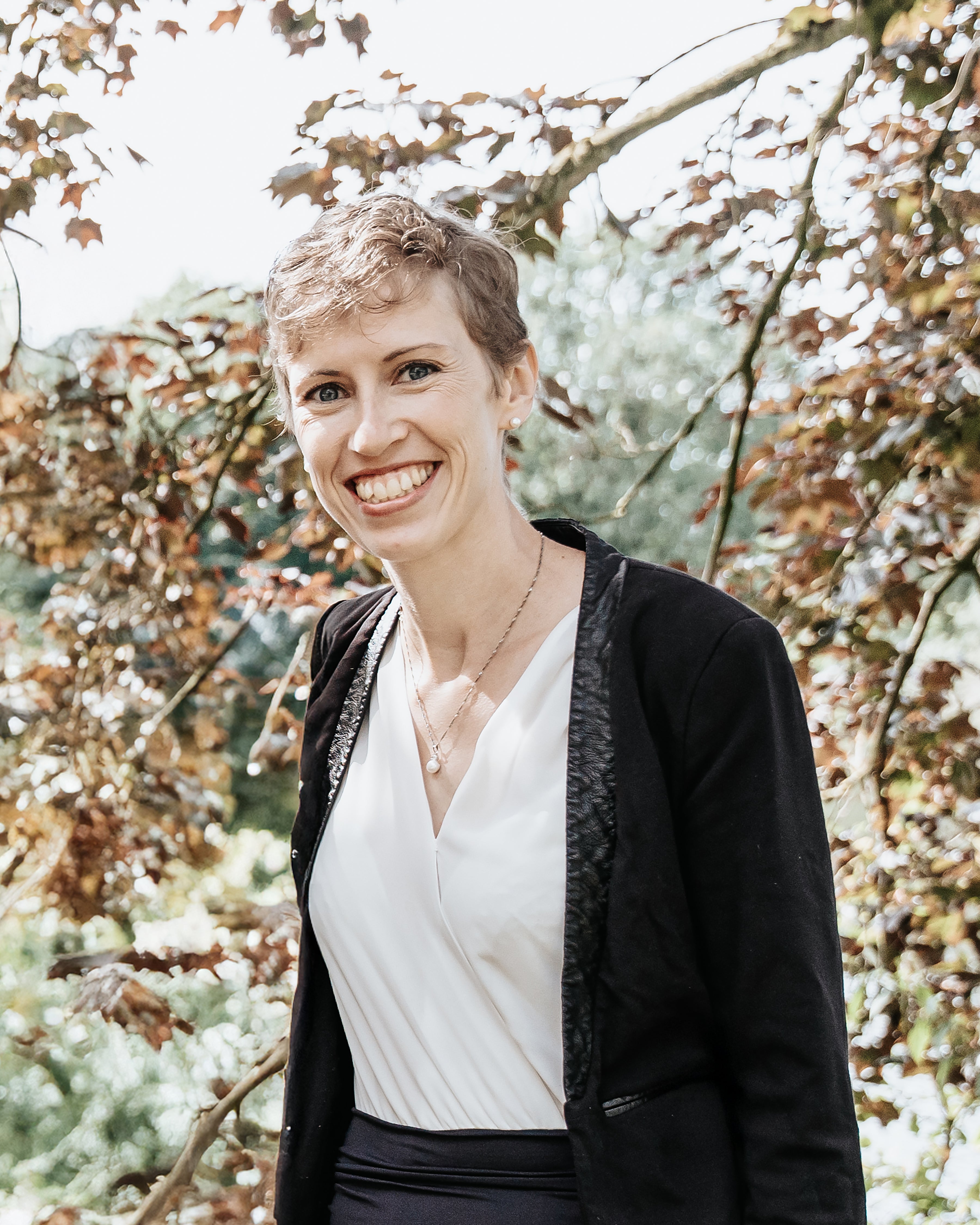 Eine Frau lächelt in die Kamera, im Hintergrund sieht man einen Baum