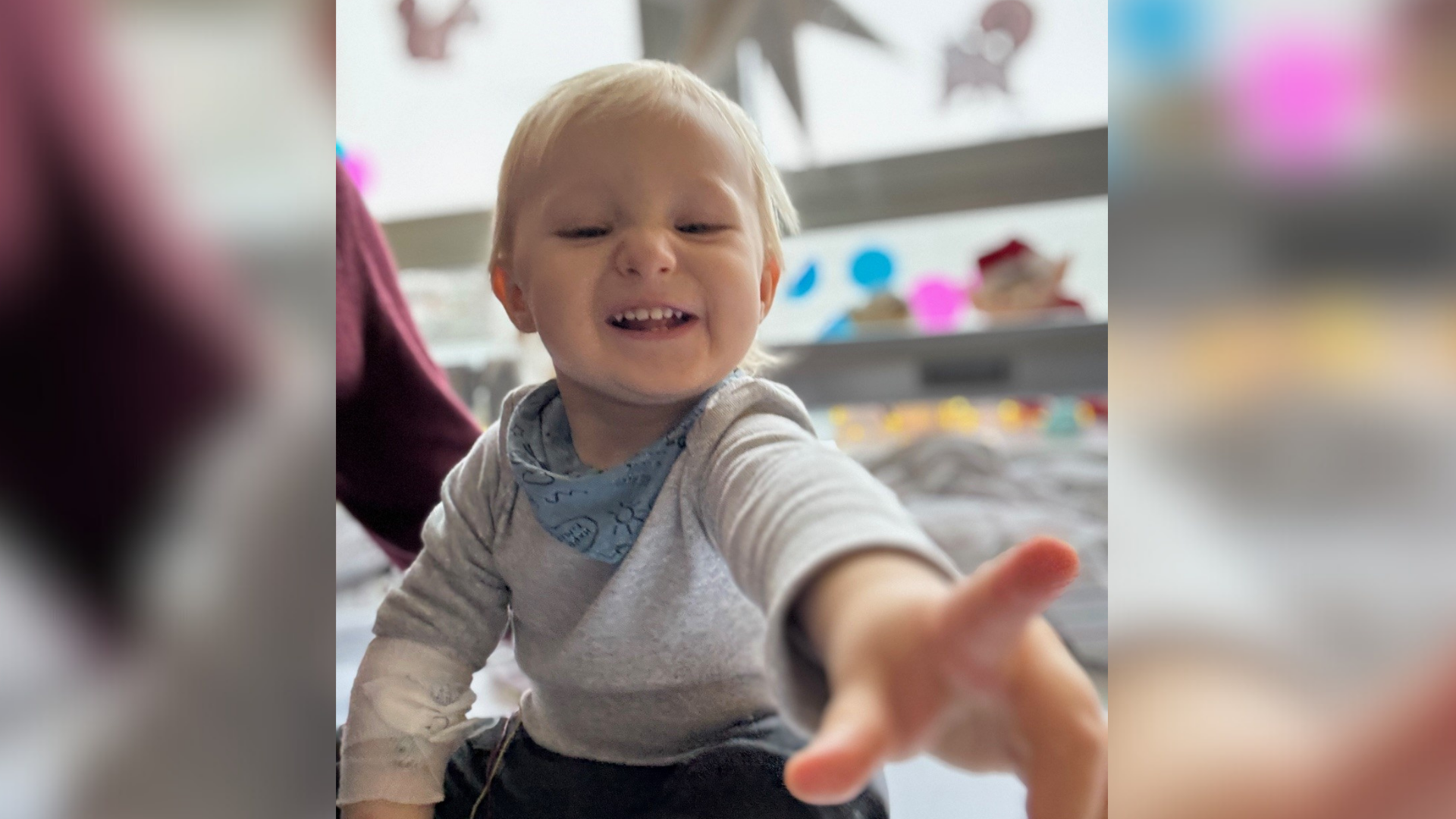 Ein lachendes Kleinkind hält den Zeigefinger in Richtung der Kamera. 