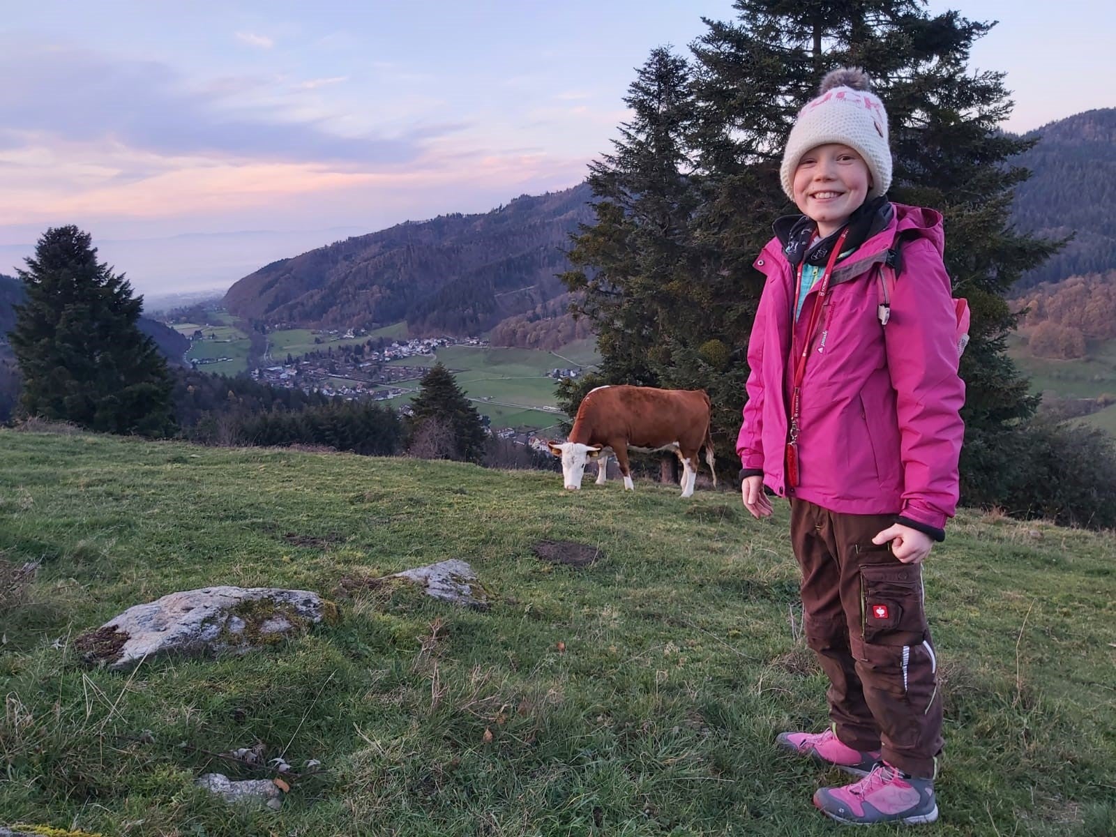 Jana auf einer Wiese, im Hintergrund eine Kuh und ein Berg