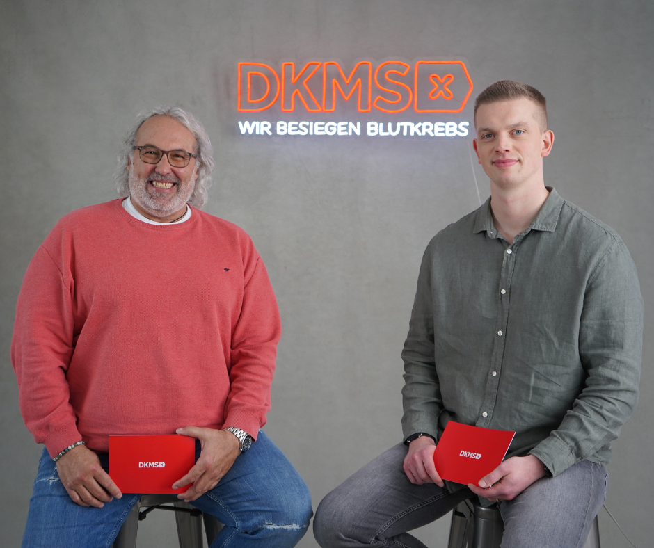 Zwei Männer sitzen auf Hockern und halten rote Aktenordner