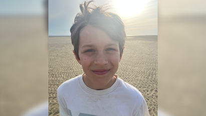 Ein Junge steht am Strand und lacht in die Kamera. 