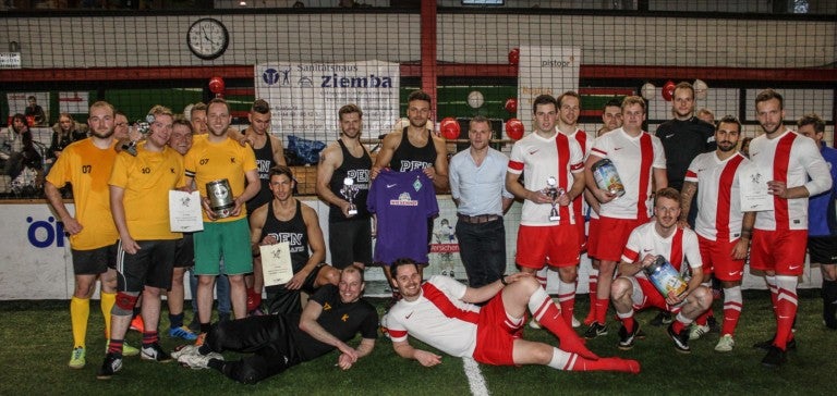 Eine Gruppe von Männern posiert für ein Foto. Sie tragen Sportkleidung und stehen auf einem Spielfeld