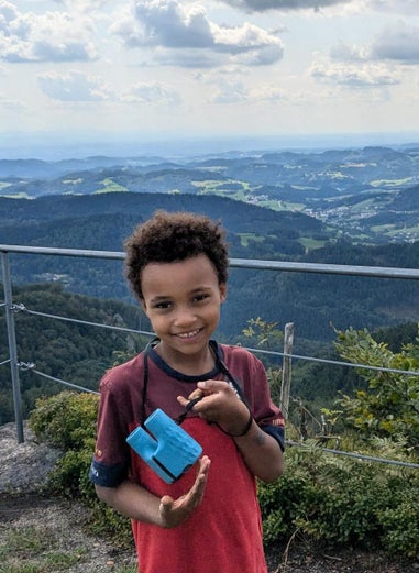 Ein Junge steht im Grünen mit einer Hügellandschaft im Hintergrund